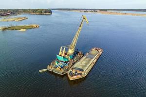 aerial view on crane extracts minerals from bottom onto huge barge in middle of lake or sea photo