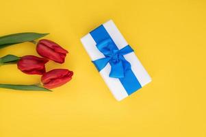 Top view of yellow table with gift box with blue ribbon and tulips. photo