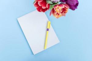 parte superior ver de un azul mesa. el bolígrafo mentiras en un blanco sábana de cuaderno. tulipanes en el mesa foto