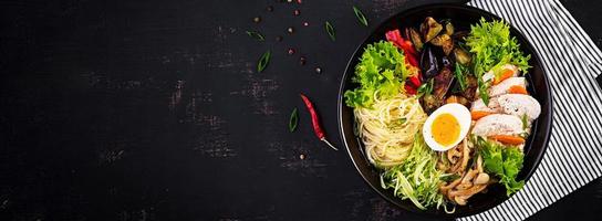 Japanese ramen soup with chicken, egg, shimeji mushrooms and eggplants on dark wooden background. Chanko nabe, sumo soup. Banner. Top view photo