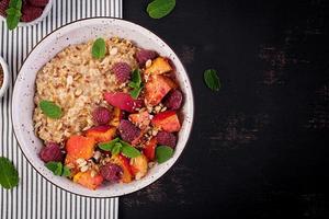 Oatmeal porridge with raspberry and peach on dark background. Healthy breakfast. Vegetarian food. Top view photo