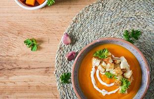 Pumpkin soup in a bowl served with parsley and croutons. Vegan soup. Thanksgiving day food. Halloween meal. Top view photo