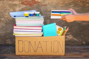 Donation box with school supplies on old wooden background. photo