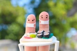 Fingers art of Happy couple in medical mask from COVID-2019. Man and woman eat sushi in cafe. photo