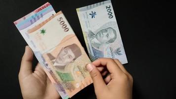 de man visar de senast problem av indonesiska sedlar, varierar från 1 000 till 100 000 nominell. rupiah valuta konceptuell isolerat på en svart bakgrund. video