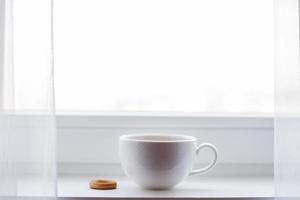 white cup with tea stands on the windowsill on the window photo
