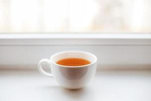 blanco taza con té soportes en el antepecho en el ventana foto