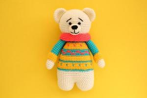 Crochet amigurumi handmade stuffed soft teddy bear toy in colored sweater on yellow background. Handwork, hobby. Craft diy newborn pregnancy concept. Knitted doll for little baby. Closeup flat lay out photo