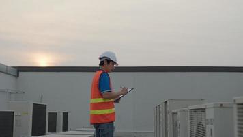 Asian maintenance engineer works on the roof of factory. contractor inspect compressor system and plans installation of air condition systems in construction. technology, online checking, mobile video