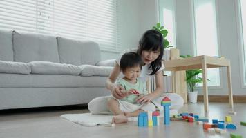 feliz Ásia mãe jogar e aprender brinquedo blocos com a pequeno garota. engraçado família é feliz e animado dentro a casa. mãe e filha tendo Diversão gastos Tempo junto. feriado, atividade, desenvolvimento video