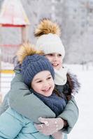 Two smiling girls in warm clothes are hugging in a snowy city. Winter walks, lifestyle. Vertical view photo