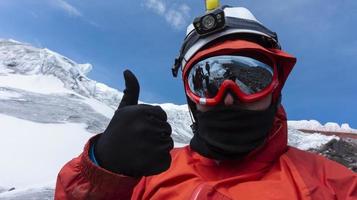 Climber with helmet, headlamp and black jacket taking a selfie on a glacier, landscape reflected in red framed glasses photo