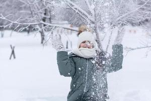 A girl in warm clothes throws snow in front of her in a winter park. Winter lifestyle portrait