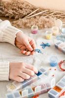 The girl's hands are weaving a dolphin on a table with items for beading. Development of creative skills and fine motor skills for children. Top and vertical view. photo