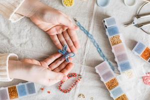 un con cuentas mariposa en el manos de un niña y artículos para trabajo de perlas en el mesa. desarrollo de creativo habilidades y multa motor habilidades para niños. parte superior vista. foto