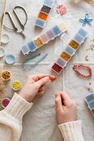 The girl's hands are weaving a beaded bracelet and items for beading on the table. Development of creative skills and fine motor skills for children. Top and vertical view. photo