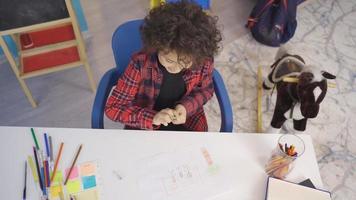 weinig jongen trekt een afbeelding Aan papier met gekleurde potloden. de kind trekt een creatief afbeelding gebruik makend van zijn verbeelding. video
