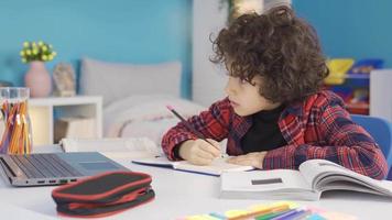 ragazzo Lavorando con il computer portatile mentre fare compiti a casa e ricerca. primario scuola alunno fare compiti a casa a il scrivania è studiando con piacere. video