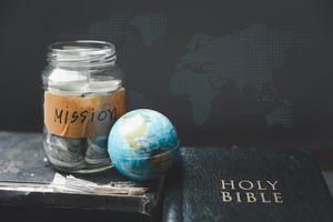 Savings jars full of money and globe with Holy Bible for mission, Mission christian idea. bible and book on wooden table, Christian background for great commission or earth day concept. photo