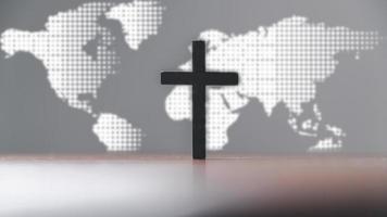 Jesus christ cross on wooden table with world map blur background. Idea of mission evangelism and gospel on world. Copy space for text, Christian background for great commission or earth day concept. photo