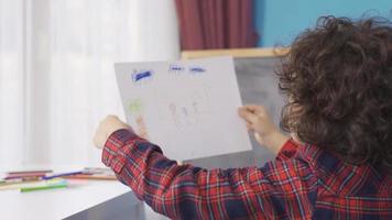 dromerig jongen tekening Bij huis. droom van wezen een schilder. weinig jongen trekt een afbeelding Aan papier met gekleurde potloden.familie afbeelding. video