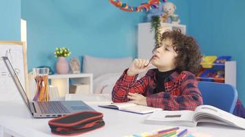 de slim jongen denkt en vondsten de antwoord naar de vraag terwijl aan het studeren. mannetje leerling aan het studeren Bij bureau aan het doen school- huiswerk en is gelukkig. video