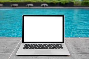 ordenador portátil con blanco pantalla para creativo diseño en piso cerca nadando piscina borde antecedentes. computadora cuaderno con monitor recorte camino para presente aterrizaje página diseño. ordenador portátil computadora burlarse de arriba modelo foto