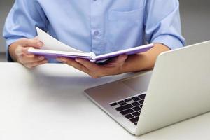 Close up hand of businessperson are opening a read book and laptop in front. Concept of business and data validation. photo