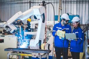 Two engineers mechanic using computer controller Robotic arm for welding steel in steel factory workshop. Industry robot programming software for automated manufacturing technology photo