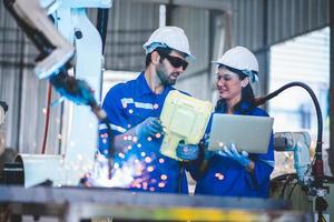 Two engineers mechanic using computer controller Robotic arm for welding steel in steel factory workshop. Industry robot programming software for automated manufacturing technology photo