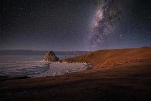 Landscape of Shamanka rock and milky way on sky with natural breaking ice in frozen water on Lake Baikal, Siberia, Russia. photo