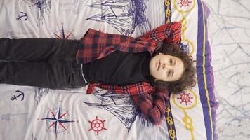 Curly haired boy using his imagination. Boy lying on his bed dreams, imagining what will happen in the future. video