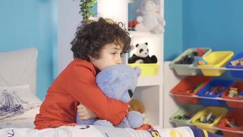 The boy who is alone in the room is afraid. The boy is scared in the nursery and hugs his cute teddy bear and looks around. video