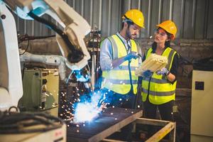 Two engineers mechanic using computer controller Robotic arm for welding steel in steel factory workshop. Industry robot programming software for automated manufacturing technology photo