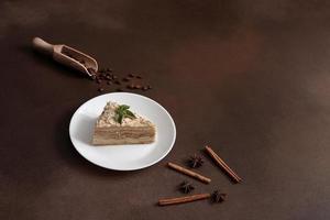 Delicious Napoleon Cake with cream on a white plate decorated with a sprig of mint on a Brown Background. A cinnamon stick, badyan, coffee beans on a brown background. Copy space photo