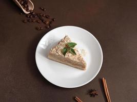 Layered Cake with cream Napoleon with mint on Brown background. A cinnamon stick, badyan, coffee beans on a brown background. Copy space photo