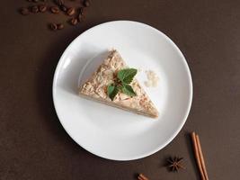 Top view of Delicious Napoleon Cake with cream on a white plate decorated with a sprig of mint on a Brown Background. A cinnamon stick, badyan, coffee beans on a brown background. Copy space photo