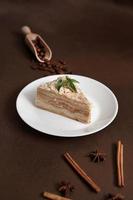 Delicious Napoleon Cake with cream on a white plate decorated with a sprig of mint on a Brown Background. A cinnamon stick, badyan, coffee beans on a brown background. Copy space photo