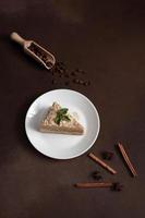 Delicious Napoleon Cake with cream on a white plate decorated with a sprig of mint on a Brown Background. A cinnamon stick, badyan, coffee beans on a brown background. Copy space photo