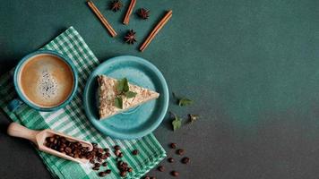 parte superior ver de delicioso Napoleón pastel con crema en un turquesa plato decorado con un puntilla de menta en un verde antecedentes. un taza de caliente café, canela palo, badyan, café frijoles en un verde fondo foto