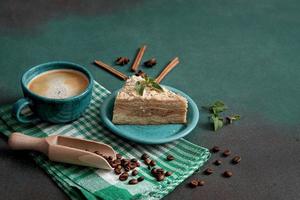 Fresh delicious Cake Napoleon with cream on a green background. A cup of hot coffee, cinnamon stick, badyan, coffee beans on a green background. Copy space photo