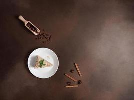 Top view of Delicious Napoleon Cake with cream on a white plate decorated with a sprig of mint on a Brown Background. A cinnamon stick, badyan, coffee beans on a brown background. Copy space photo
