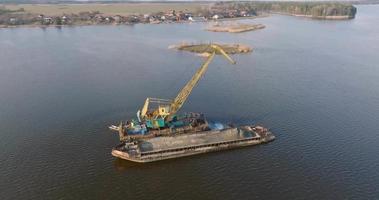 circular flight and aerial view on crane extracts minerals from bottom onto huge barge in middle of lake or sea video