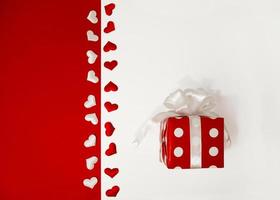 Gift in a red box, tied with satin ribbon on a red and white background with hearts. Holidays and greeting cards. photo