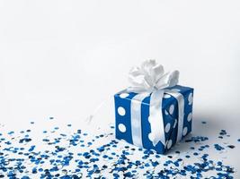 Blue gift box with bow on white background with confetti. The color of 2020 is classic blue. photo