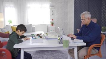 padre y hijo estudiar juntos a hogar. padre y hijo a hogar, el niño sorteos, y el padre trabajos con un ordenador portátil. video