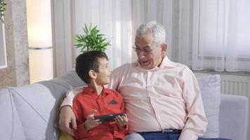 père et fils sont en riant et à la recherche à quelque chose amusement sur le téléphone. père et fils en train de regarder marrant vidéos sur le téléphone à maison. video