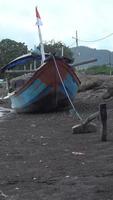 a fishing boat, with the Indonesian flag anchored on the bank of the estuary - stock vertical video