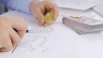 Businessman is analyzing and working on bitcoin chart. Man analyzing bitcoin chart on table holds bitcoin in hand. video