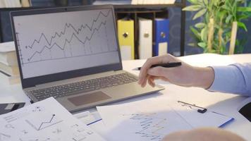 Businessman Works With Graph Data. Financial charts on a laptop and statistics printed on paper. video
